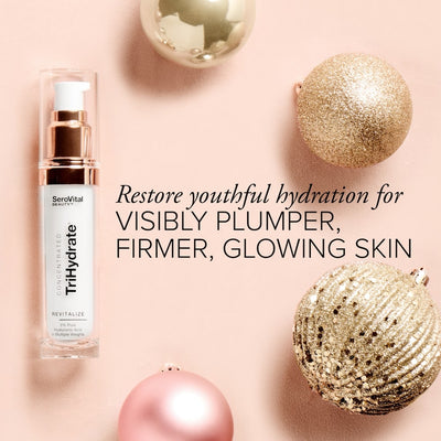 A bottle of hyaluronic acid serum TriHdyrate on a pink background with holiday ornaments and text that says Restore youthful hydration for visibly plumper, firmer, glowing skin