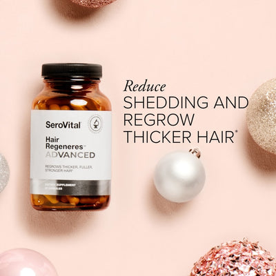 A glass bottle of Hair Regeneres ADVANCED on a pink background with holiday ornaments and text that says Reduce shedding and regrow thicker hair