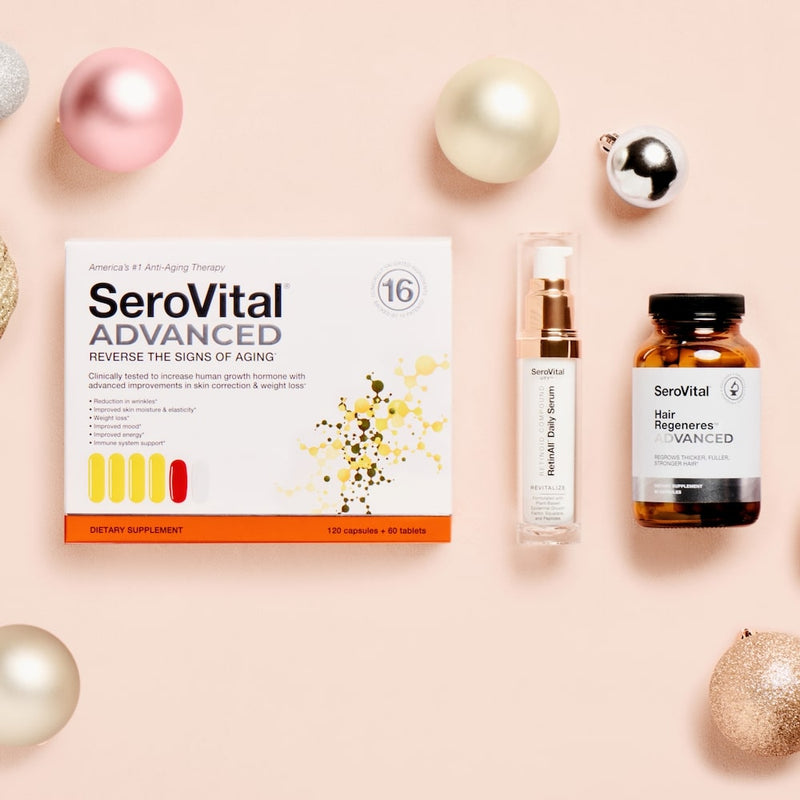 A box of anti-aging supplement SeroVital ADVANCED on a pink background next to a bottle of anti-wrinkle serum RetinAll Daily Serum and hair growth supplement Hair Regeneres ADVANCED, with festive holiday ornaments in the background