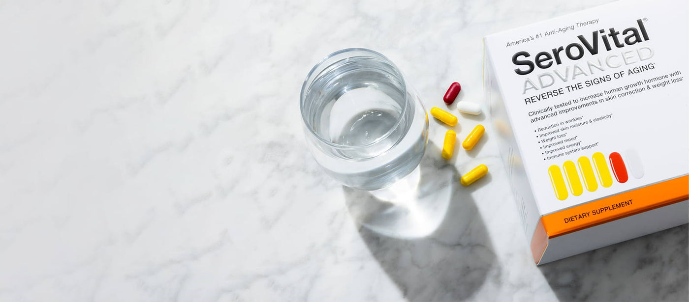 A box of SeroVital ADVANCED, which reverses the signs of aging, on a white marble countertop next to a glass of water with 4 yellow capsules, 1 red capsule and 1 white capsule